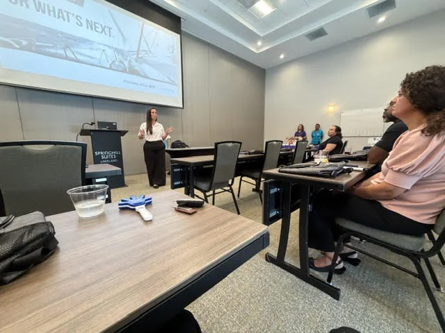 A presenter speaking near a podium to attendees seated at tables in a conference room at SpringHill Suites Lakeland.